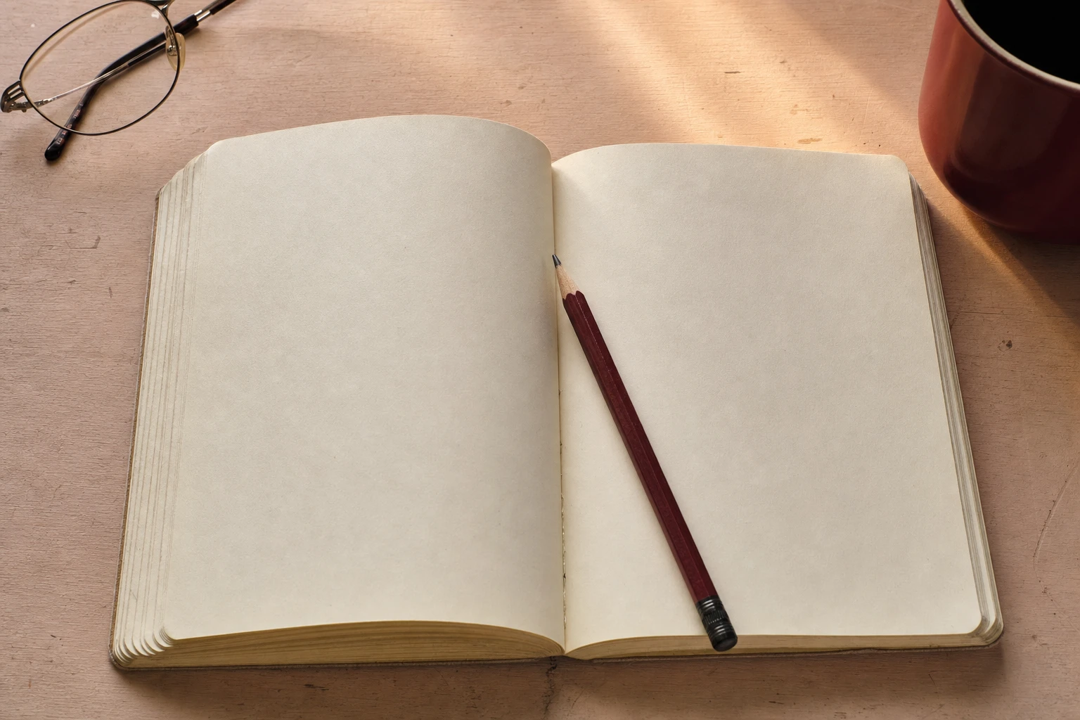 An open notebook, wine-red pencil and reading glasses on a quiet desk